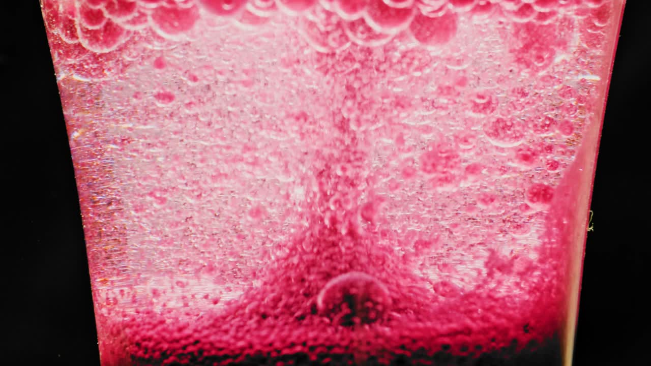 밝은 배경과 약간의 더 큰 거품이 떨어지는 유리에서 반짝이는 붉은 거품의 매크로 샷