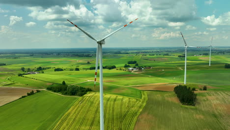 Aerial-footage-featuring-several-wind-turbines-standing-tall-over-green-agricultural-fields-under-a-bright,-partly-cloudy-sky