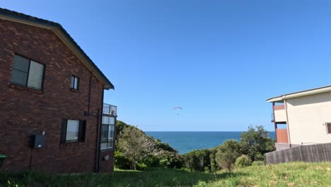 paragliders soaring over the ocean near coastal houses