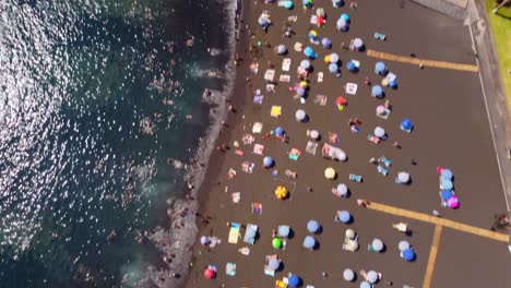 Una-Vista-Aérea-De-La-Playa-De-Tenerife-Santiago-Con-El-Agua-Azul-Del-Mar-A-Un-Lado-Los-Edificios-Están-Al-Otro-Lado-En-España-A-La-Luz-Del-Día