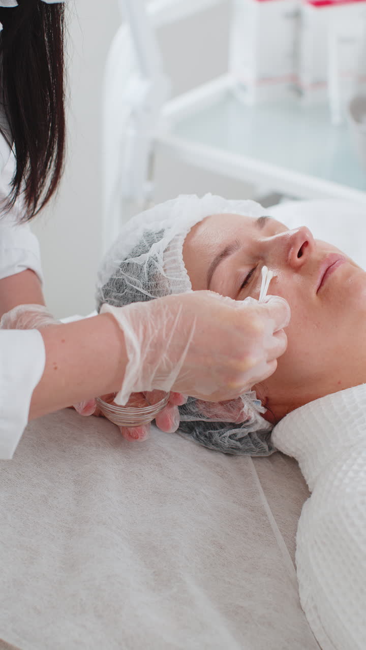 Estetista che applica una maschera idratante per peeling chimico medico acido sul viso e sugli occhi di una giovane donna.
