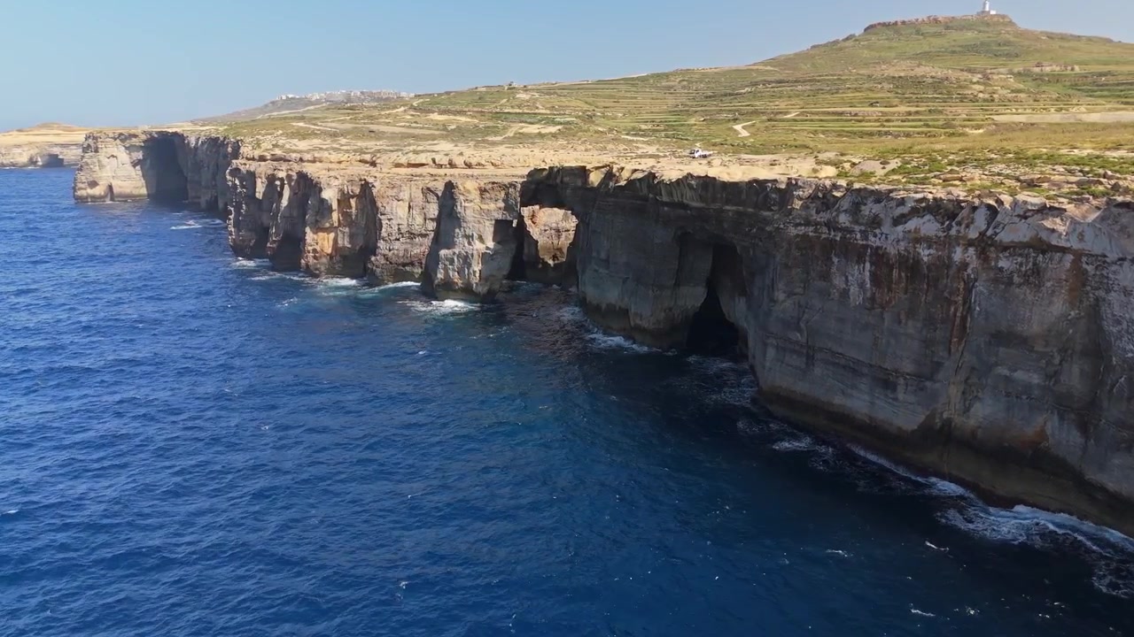 Wied il-Mielaħ på Gozo, Malta, en naturlig steinbue og kystklipper over Middelhavet med bølger og blått vann langs den ulendte kystlinjen, tatt med drone