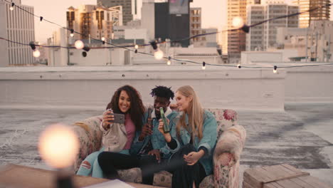 happy multi ethnic friends enjoying rooftop party drinking alcohol taking selfie photos using smartphone sharing fun weekend on social media at sunset