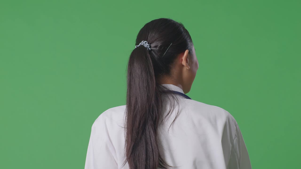 스테토스코프를 들고 있는 아시아 여성 의사가 병원 안의 녹색 스크린 배경에서 돌아다니고 있는 모습