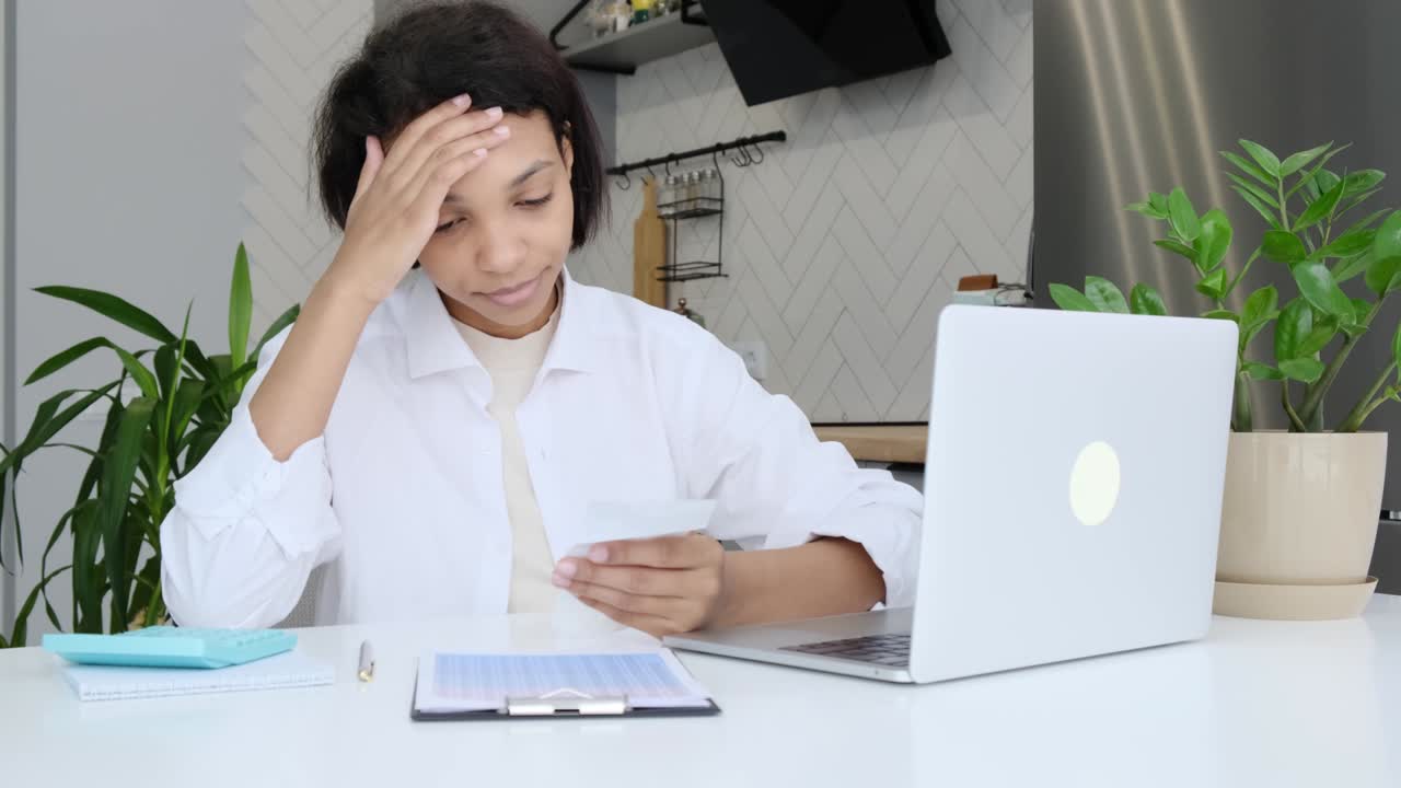 안경을 쓴 젊은 아프리카계 미국인 여성은 종이 서류를 살펴보고, 비즈니스 업무를 관리하고, 세금을 요약하고, 미래 투자를 계획하고, 가정 사무실에서 혼자 회계를합니다.