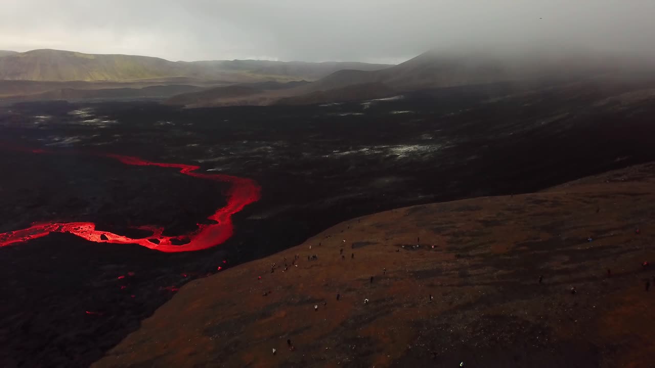 vista aérea de personas mirando la erupción del volcán fagradalsfjall, con lava fluyendo por el suelo del valle de meradalir