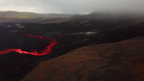 Vista-Aérea-De-Personas-Mirando-La-Erupción-Del-Volcán-Fagradalsfjall,-Con-Lava-Fluyendo-Por-El-Suelo-Del-Valle-De-Meradalir