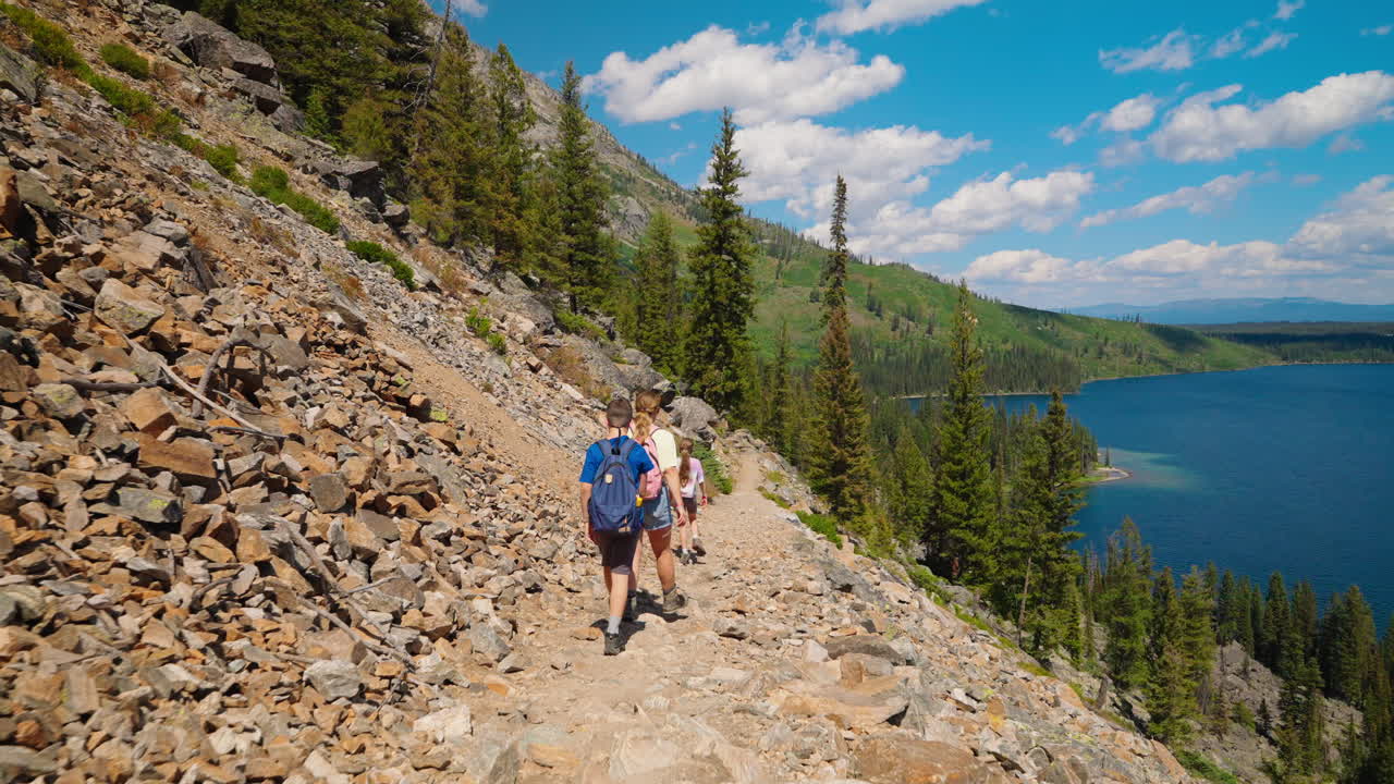 Hikers on a scenic mountain trail overlooking a large blue lake