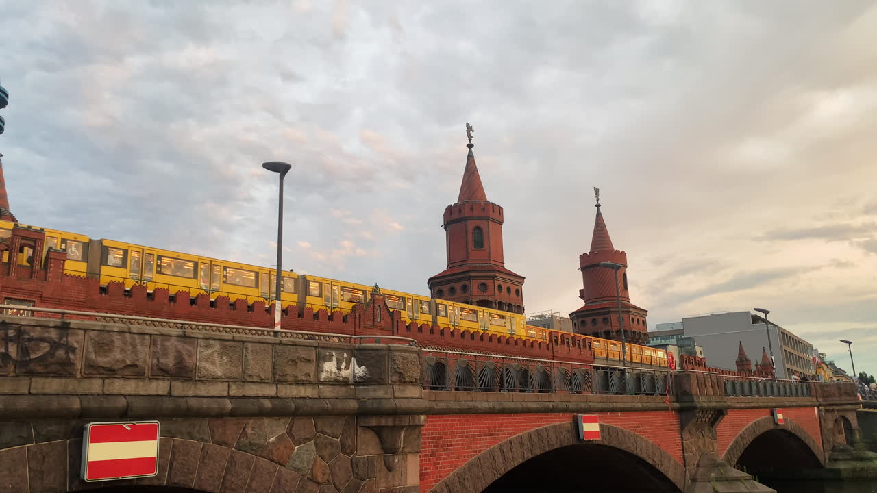 Steady clip of a red brick bridge in Berling with two castle belltowers in the background and traffic on the bridge