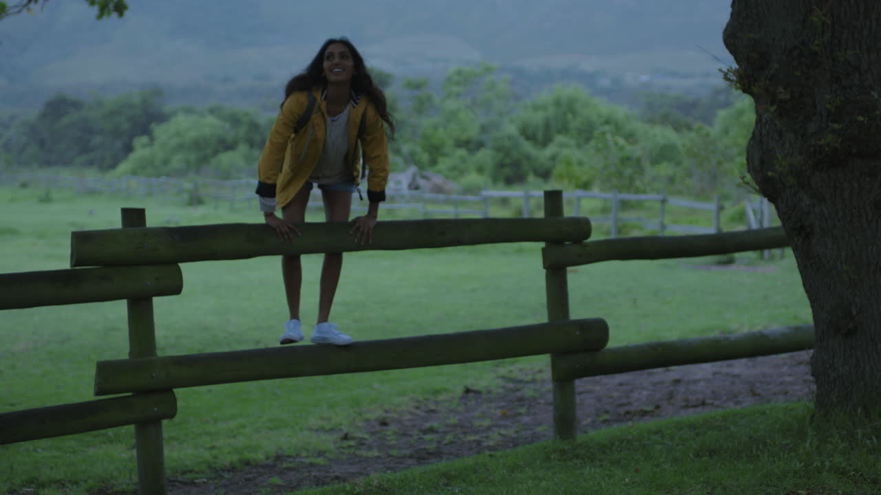 giovane donna indiana indipendente seduta sulla recinzione godendo di una bella campagna verde fattoria sorridente allegra contemplazione riposando sotto l'albero