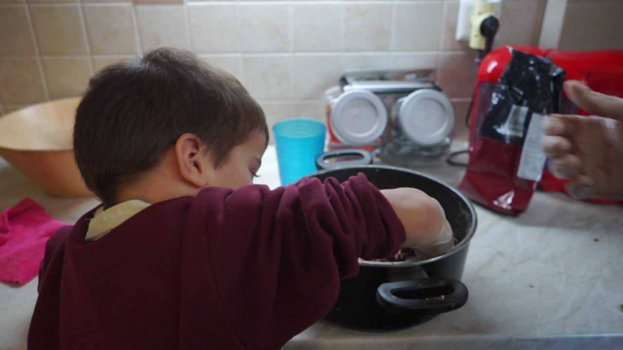 Caucasian toddler boy helping his mother making energy bars in the kitchen