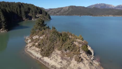 Orbit-Aerial-view-of-a-mountain-lake-islet-sunny-winter-day-Peaks-background