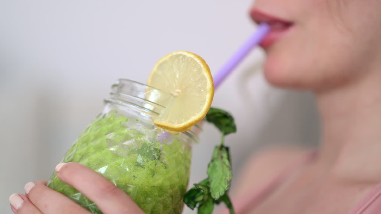 Close up of a woman drinking a green juice while sitting on a couch