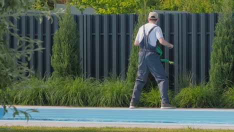 jardinero regando plantas cerca de la piscina