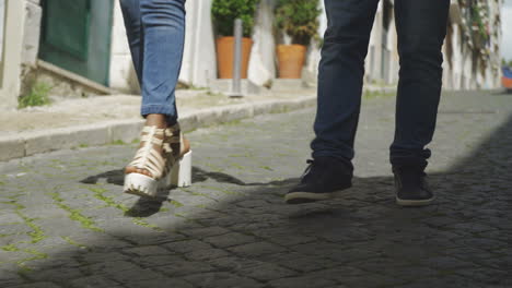 legs of young people walking on paved sidewalk.