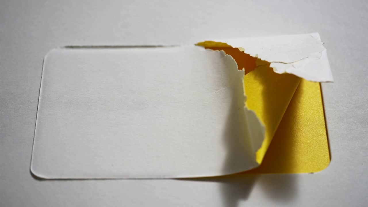 Peeling white peelable label top-right corner after tear on gray table, revealing gold foil backing
