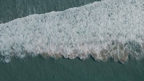 turquoise foaming ocean breaking against sandy shore aerial top down view above surf