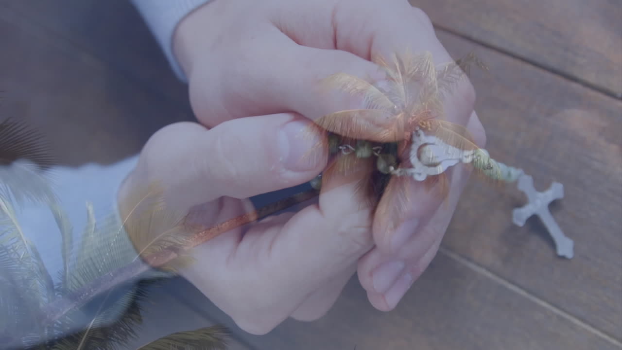 Holding rosary beads, hands overlaid with palm trees creating serene animation