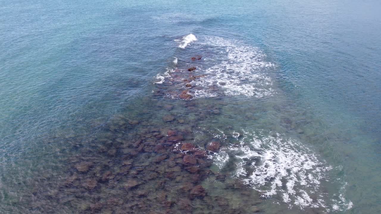 Aerial of shallow clear ocean sea water, pebble stones view, light waves