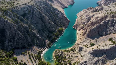 aerial top down shot of mediterranean bay with parking boats surrounded by mountains in sunlight - jablanac, croatia