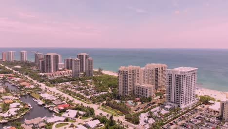 a drone shot flying backwards captures a beachfront hotel at sunset, revealing the sandy shores, ocean waves, and the hotel’s pool under a golden sky.