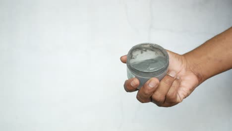 hand holding a jar of grey cosmetic clay mask