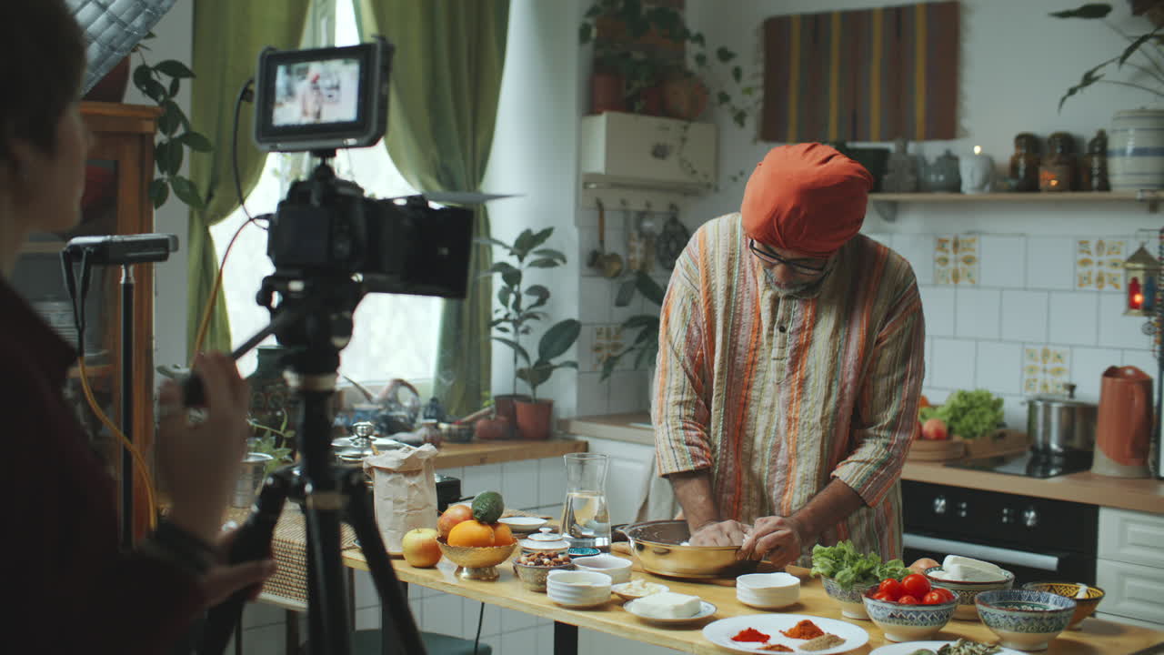 Food blogger indiano con turbante e kurta che spiega una ricetta alla telecamera in cucina