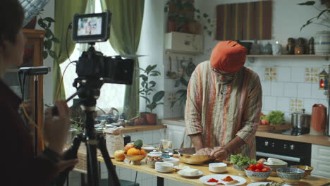 indian food blogger in turban and kurta explaining recipe to camera in kitchen