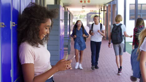 una adolescente negra usando un teléfono inteligente en el corredor de la escuela