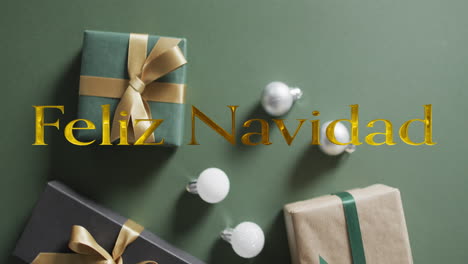 feliz navidad text in gold over christmas baubles and presents on green background