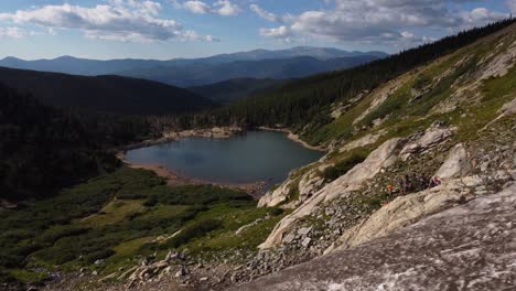 Flying-past-snow-shelf-to-view-snowmelt-lake-and-mountains-in-Colorado,-aerial