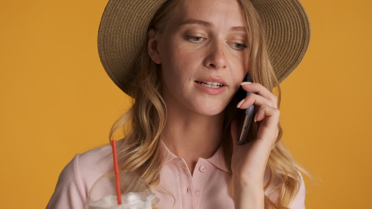 Kaukasisk kvinde taler i telefon, mens hun drikker iskaffe