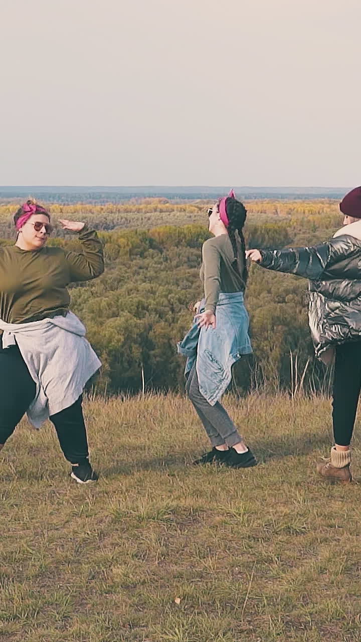 joyful young women dance at tent in touristic camp on steep river bank against pictorial landscape in autumn slow motion