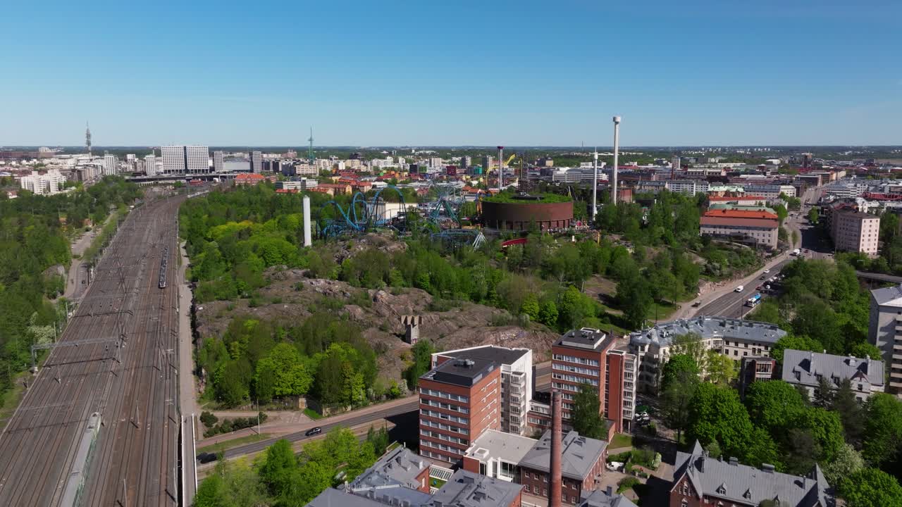 Drone stiger op over tomme togskinner for at vise Helsinki, Finland med frodige grønne træer