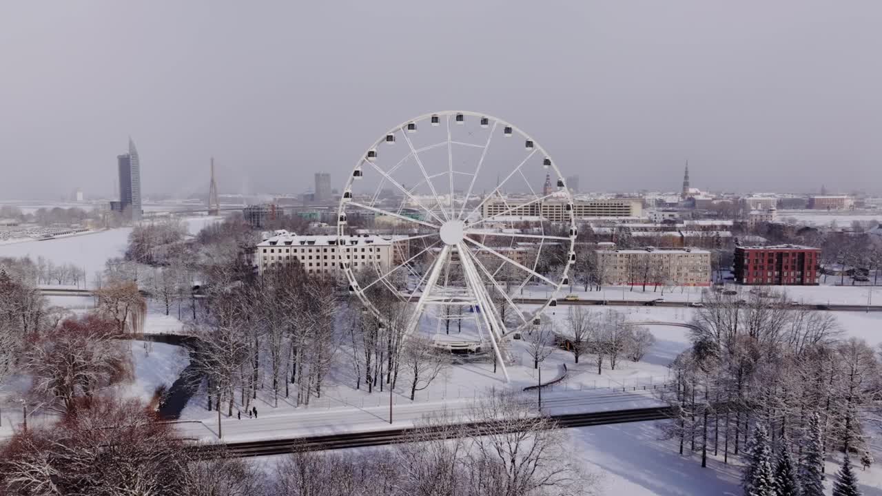 Real time drone shot flying past snowy Ferris wheel and Riga skyline in winter