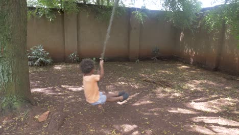 a young mixed raced boy swinging on a rope swing in backyard