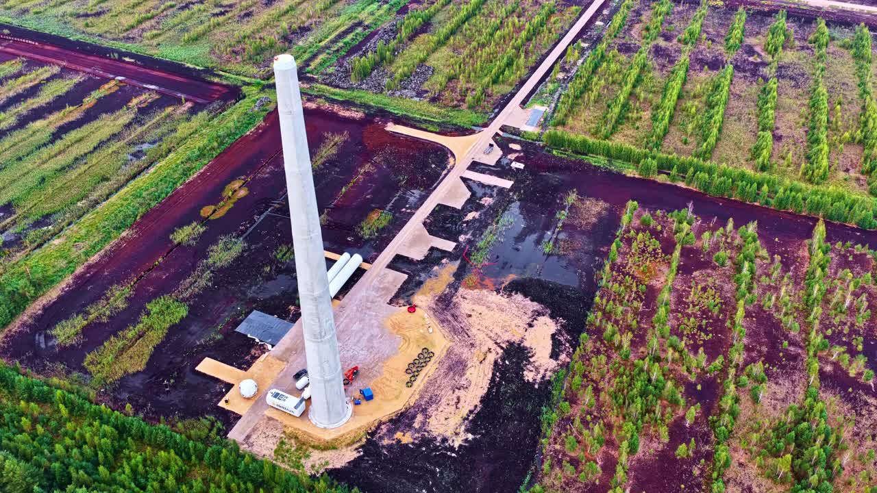 A wind turbine tower is being built in a bog, surrounded by muddy terrain and access roads