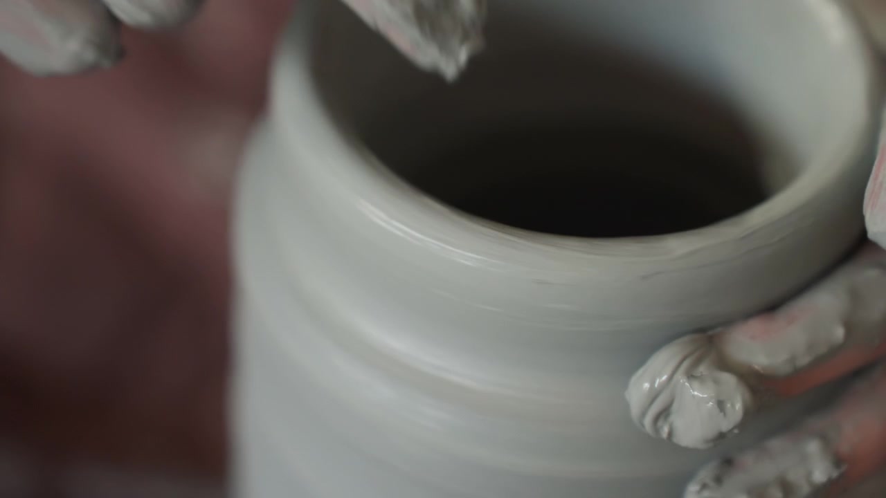 Sculptor delicately forms pottery on spinning wheel. Close view of hands shaping moist gray clay on rotating wheel. Intimate shot capturing gentle hand movements as clay is expertly shaped on wheel