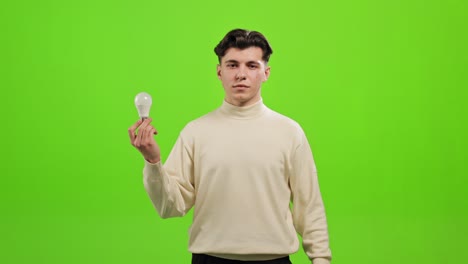 the man is standing and looking at the camera. he is raising his hand and holding the light bulb. he is standing on a green background. green screen. 4k.