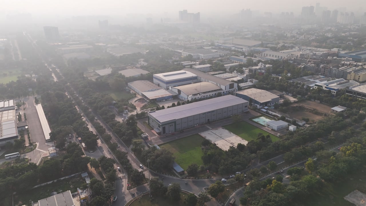 Wide aerial footage of an industrial area with warehouses and factory buildings under a hazy sky, showcasing large-scale infrastructure, urban sprawl, and visible air pollution during winter condition