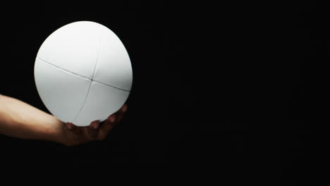 hand of african american man holding white rugby ball on black background, copy space, slow motion