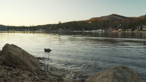 fishing pole wedged between rocks on a shoreline of a mountain lake at sunset, luxury homes in the background