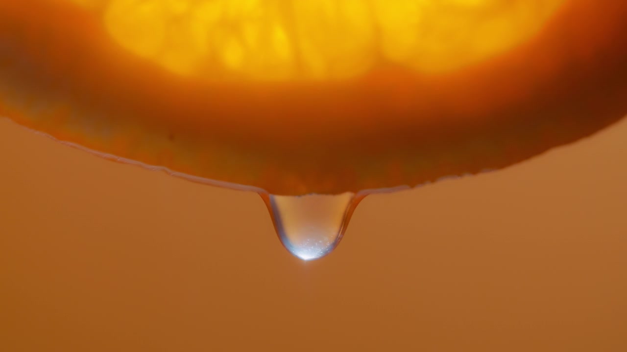 Macro shot of water droplet falling from an orange slice. Slow motion