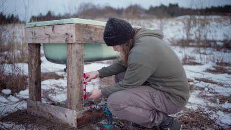 Männlicher-Arbeiter,-Der-Im-Winter-Den-Holzständer-Des-Whirlpools-Im-Freien-Nivelliert