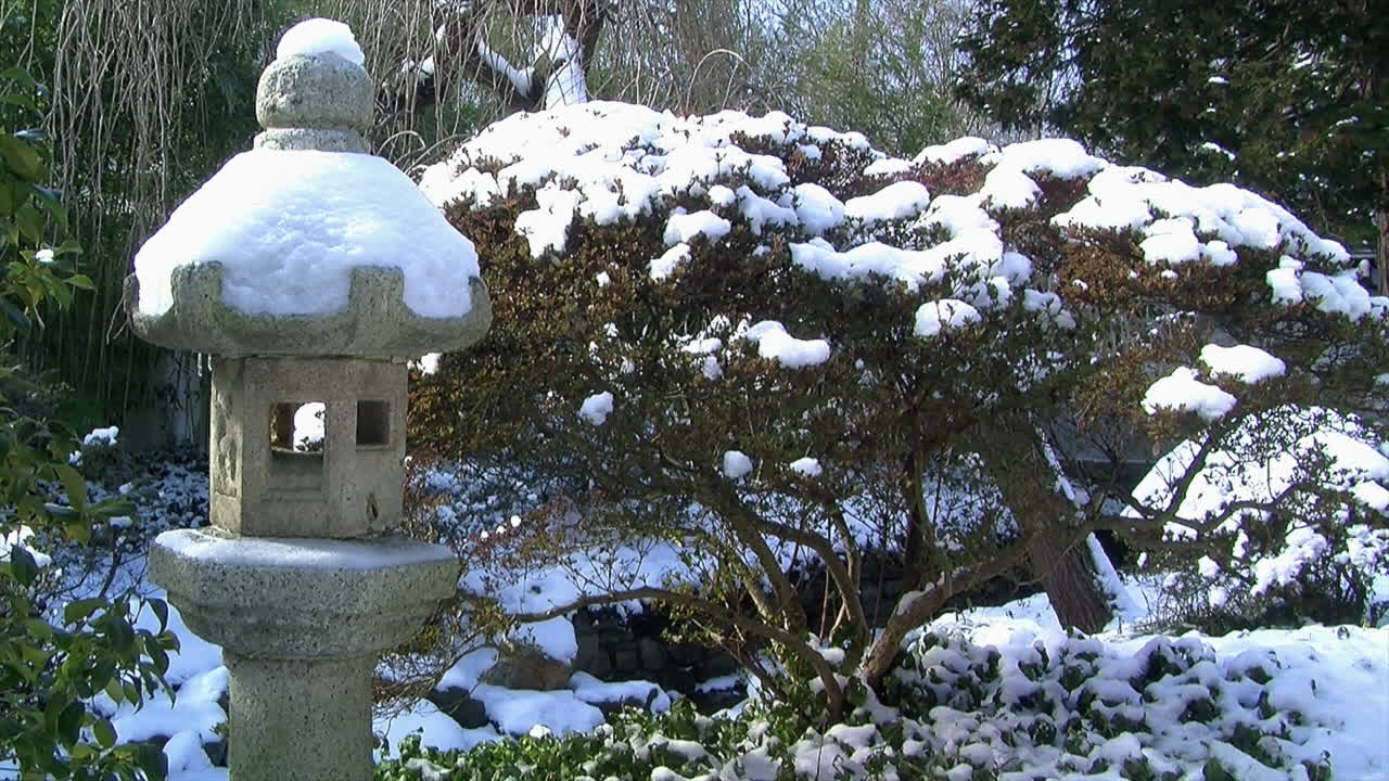 눈은 일본 정원에서 랜턴과 관목을 덮고 있습니다.