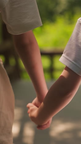 little girl holds toddler boy hand walking together along overpass in forest closeup. children enjoy summer and friendship at countryside nature