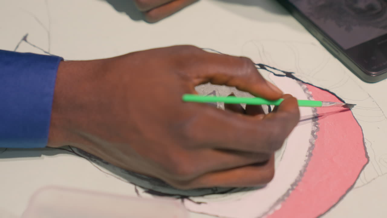 Artist swiftly outlining with bold confident strokes. Hand meticulously tracing edges of painted object on paper. Person skillfully refining contours and color blocks with precise swift movements