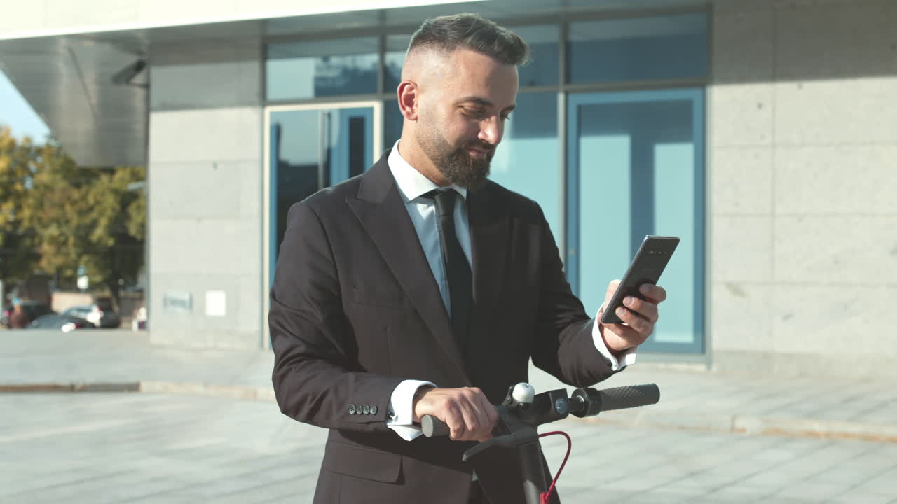 hombre de negocios usando un teléfono inteligente en un scooter eléctrico fuera de un edificio moderno