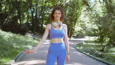 woman in blue workout clothes smiles at the camera while standing on a park path.