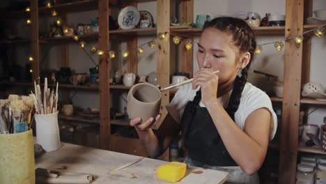 young woman smoothing out the clay cup using a wet brush